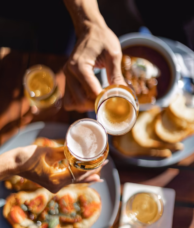 Cheers © Unsplash.com, Dorine Allali Detailaufnahme vom Anstoßen mit Biergläsern über einem Esstisch im Garten